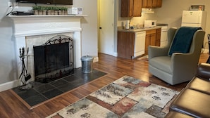 Un salón con chimenea, un televisor montado encima y una zona de estar con un sillón y un sofá.