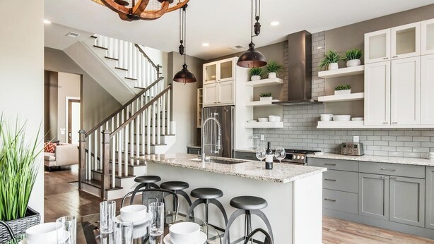 Een moderne keuken met een centraal eiland, barstoelen en een trap naar een hoger gelegen niveau.