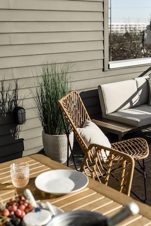 Enjoy al fresco dining on the patio with a table set for two, surrounded by lush greenery and a comfortable sofa.