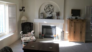 A living room with a fireplace, a floral armchair, a wooden cabinet, and a television on a stand.