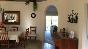 A dining area with a table, chairs, a mirror, a clock, and a view through an archway to an outdoor area.