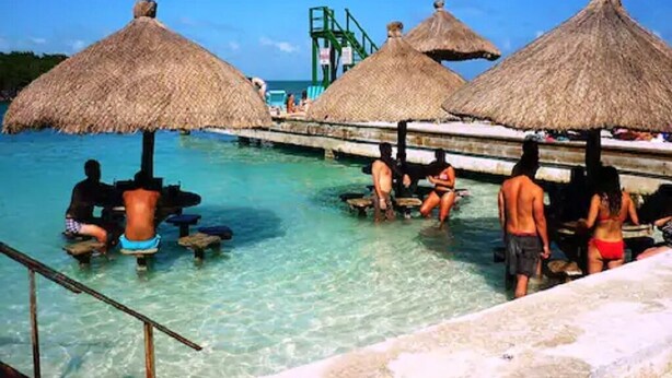 A pool area with thatched umbrellas and people in swimwear. - Oceanfront home; Rooftop deck; Fabulous views; Upper level apartment (Caye Caulker)
