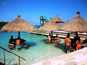 A pool area with thatched umbrellas and people in swimwear. - Oceanfront home; Rooftop deck; Fabulous views; Upper level apartment (Caye Caulker)