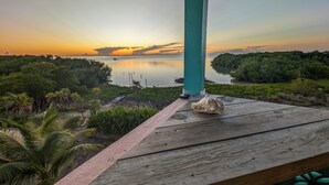 A wooden deck with a seashell, overlooking a calm body of water at sunset with a forested island in the distance. - Oceanfront home; Rooftop deck; Fabulous views; Upper level apartment (Caye Caulker)