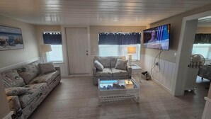 Una sala de estar con dos sofás, una mesa de centro, un televisor y una puerta.