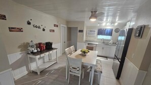 Una cocina con armarios blancos, una mesa de comedor con sillas, una cafetera y un ventilador de techo.