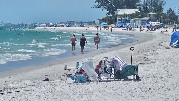 Una playa con gente caminando, carpas y sillas de playa.