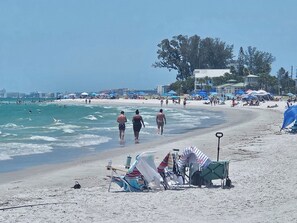 A beach with people walking, tents, and beach chairs.