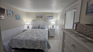 Un dormitorio con cama, mesitas de noche, cómoda, ventana con persianas y adornos en la pared.
