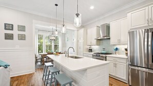 A modern kitchen with white cabinetry, stainless steel appliances, and a central island with bar stools. - WaterSound West Beach Cottage-EV Charger, SUP, Kayak (Santa Rosa Beach)