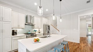 A modern kitchen with white cabinetry, a large island, and blue bar stools. - WaterSound West Beach Cottage-EV Charger, SUP, Kayak (Santa Rosa Beach)