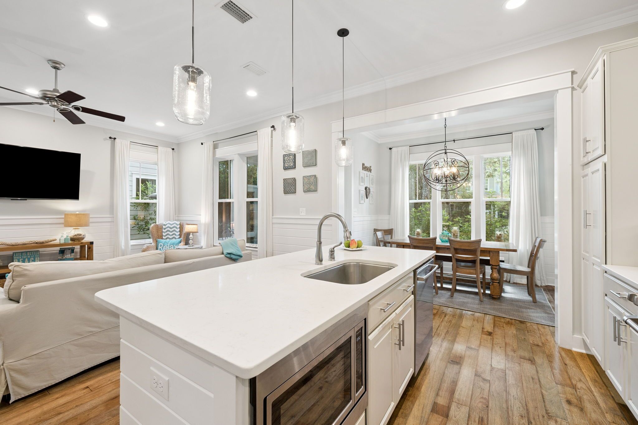 A modern kitchen with a white countertop, wooden flooring, and a dining area with a table and chairs.