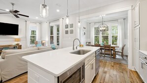 A modern kitchen with a white countertop, wooden flooring, and a dining area with a table and chairs. - WaterSound West Beach Cottage-EV Charger, SUP, Kayak (Santa Rosa Beach)