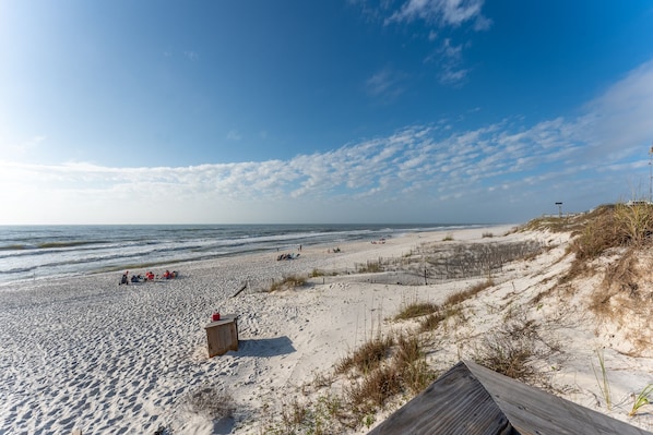 A beach with a wooden boardwalk, sandy dunes, and a clear sky.