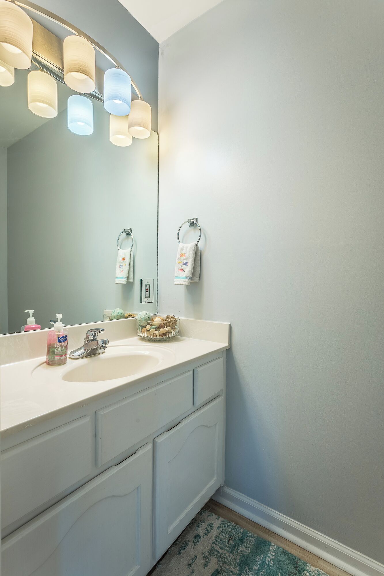 Une salle de bain avec un lavabo blanc, un miroir et un luminaire placé au-dessus.