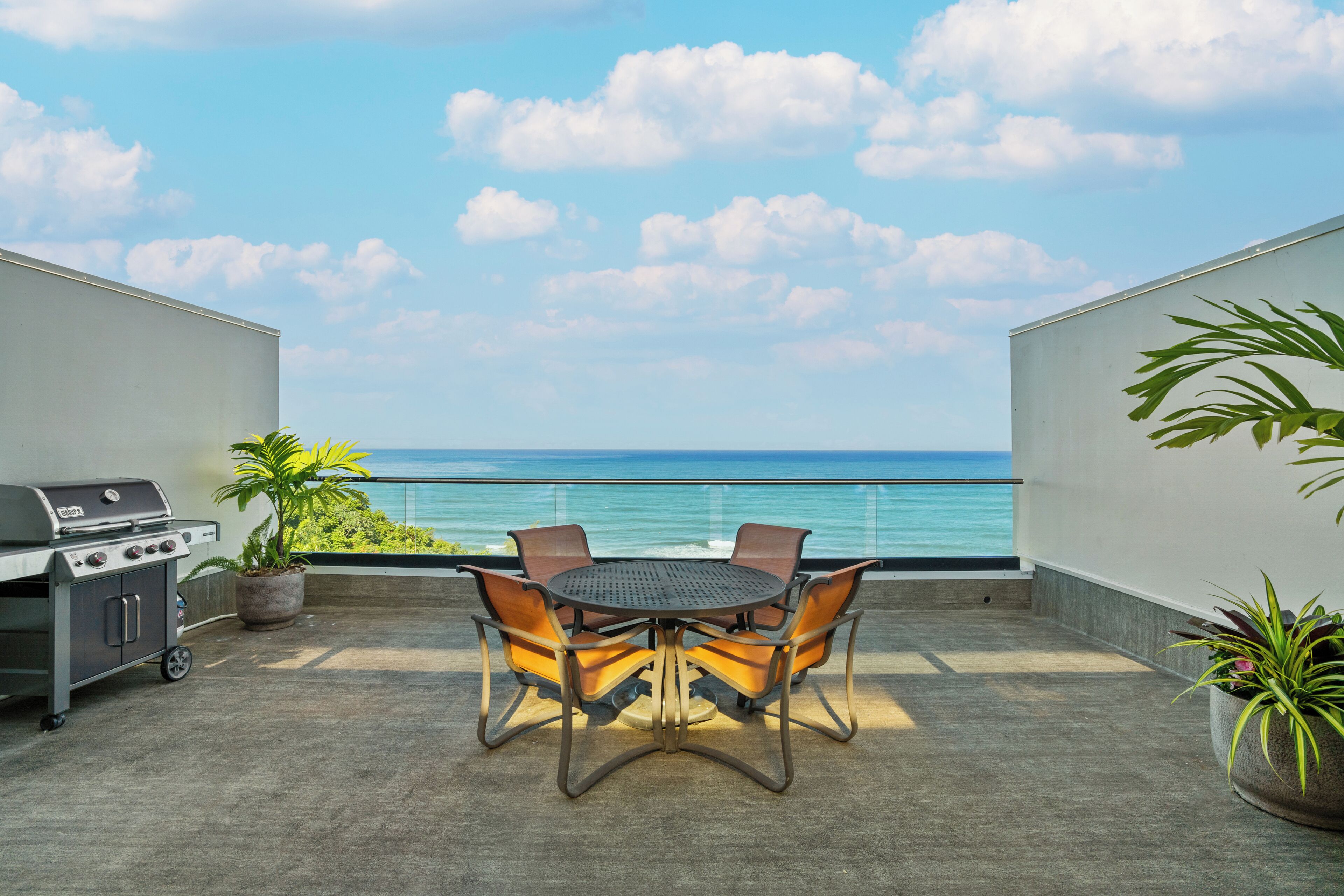 A patio with a round table and chairs, a grill, and potted plants.