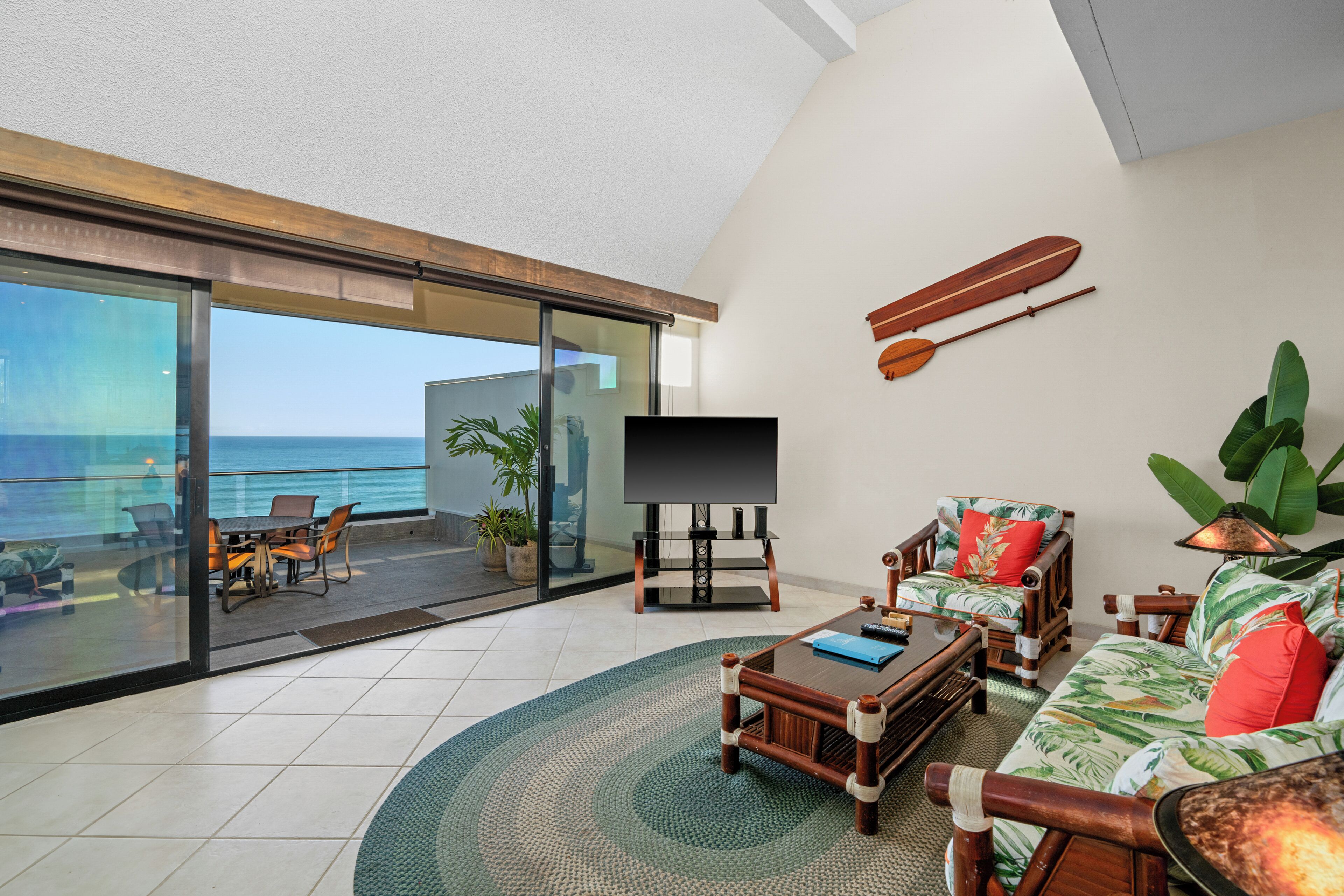 A spacious living area with a large TV, wooden furniture, and a view of the ocean.