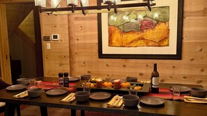 Una cuina-menjador de fusta amb una taula ben preparada per a quatre, un penjador i un quadre abstracte amb marc a la paret.