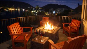 A terrace with a fire pit, two wooden chairs, and a table with wine glasses. - Relaxing Lakefront-Pool-Spa-Pontoon-Game Room-FirePits-Cardinal Stadium-WM Open (Glendale)