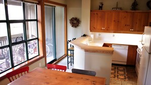 Une cuisine avec des meubles de rangement en bois, un plan de travail et un lave-vaisselle. Il y a une fenêtre avec des stores et une porte qui donne sur l’extérieur.