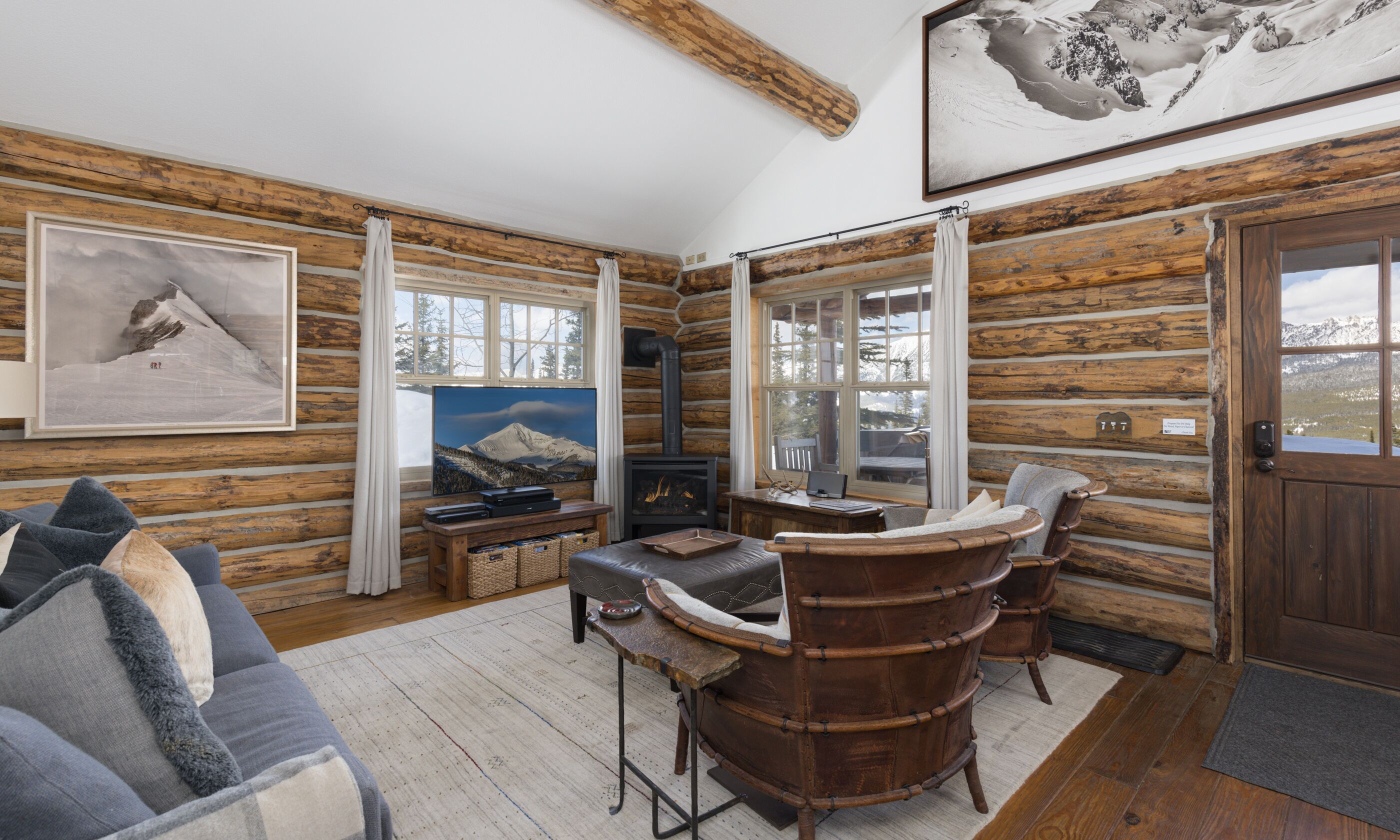 A log cabin interior with a fireplace, a sofa, a chair, and a television.