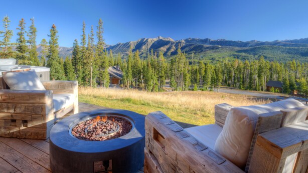 Eine Holzterrasse mit Feuerschale, Gartenmöbeln und Blick auf die Berge.