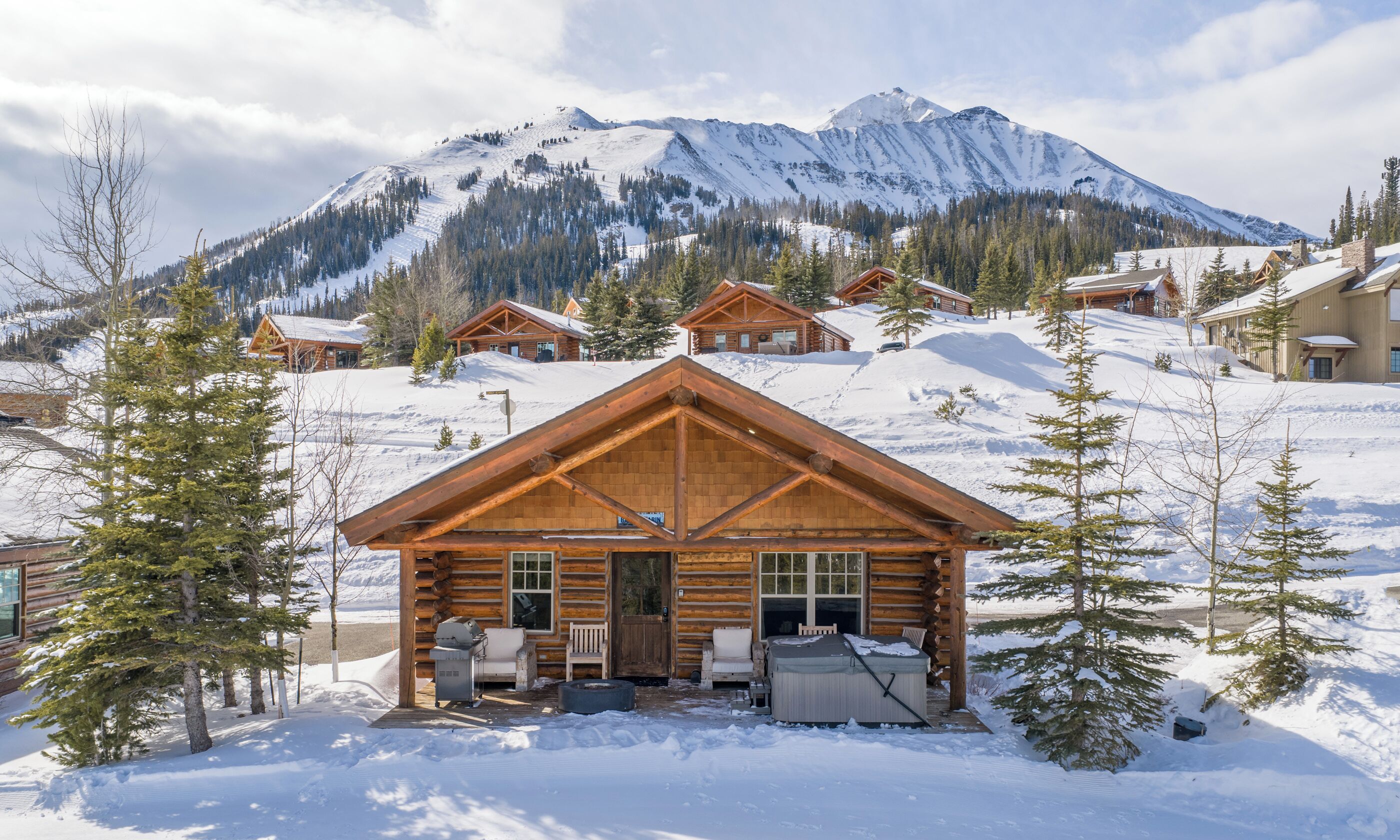 Une cabane en rondins avec un porche, un jacuzzi et un barbecue à l’extérieur.
