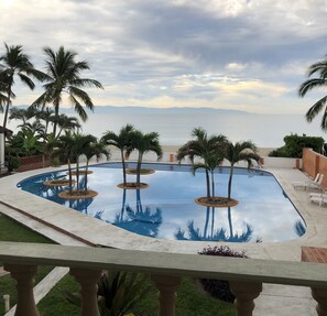 Une piscine bordée de palmiers, une vue sur la mer et un ciel nuageux.