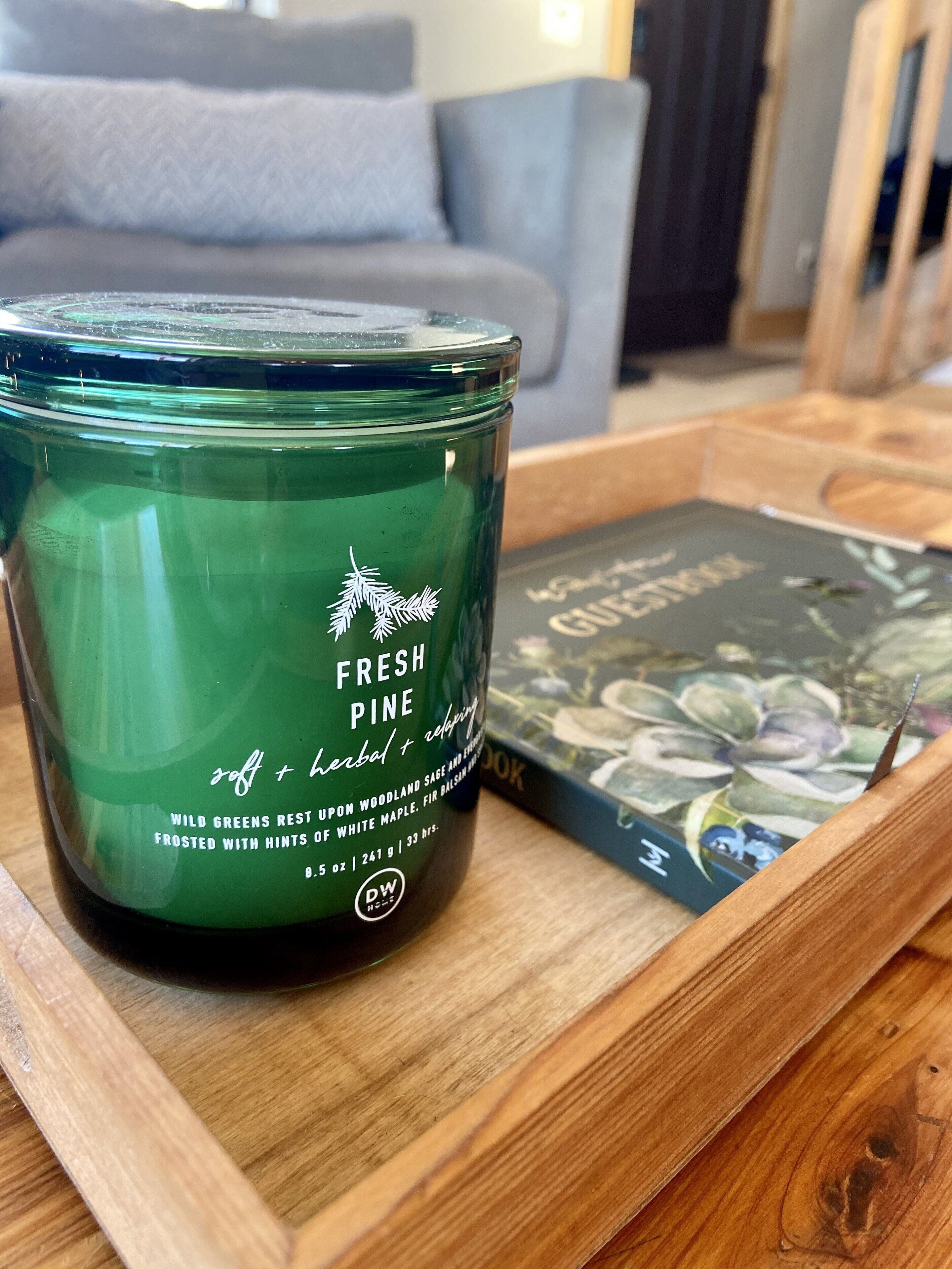 Ein grünes Kerzenlicht mit dem Aufdruck "FRESH PINE" auf einer Holzschale.