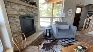 Un salón acogedor con chimenea de piedra, un sofá cómodo, una mesa de centro de madera y un tapete de cuero de vaca.