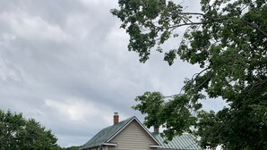 A two-story house with a green metal roof, a covered porch, and a driveway leading to the garage. - The Olde Farmhouse Spacious Lakefront House with Amazing View (Goodview)