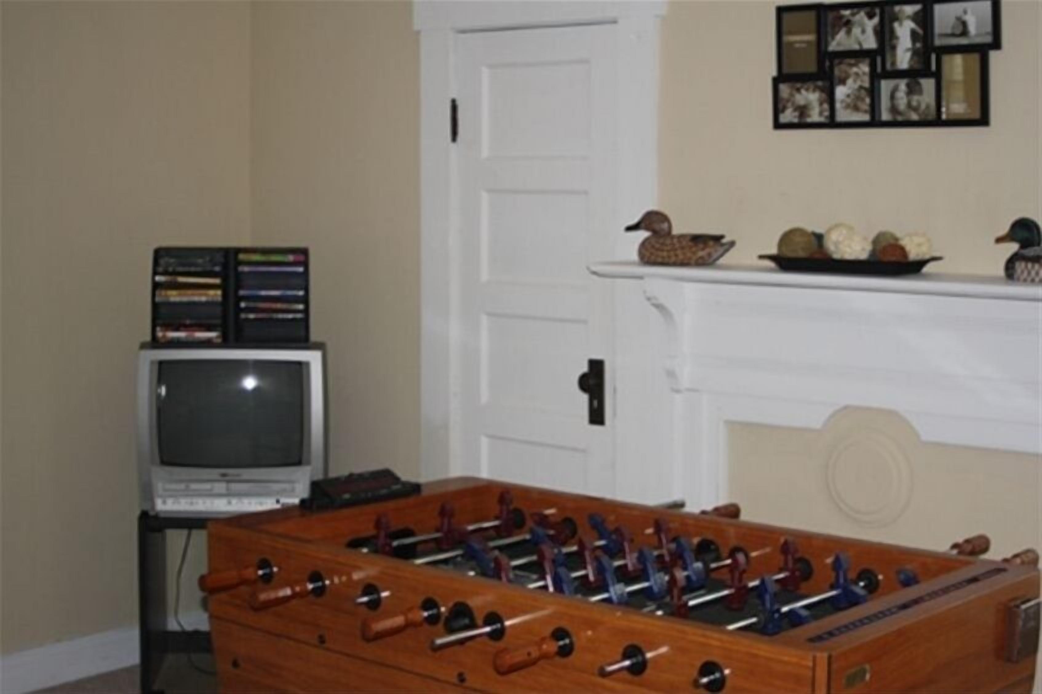 Een kamer met een houten tafelvoetbaltafel, een televisie en een schoorsteenmantel met decoratieve objecten.