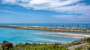 A coastal view with a clear sky, calm sea, and a rocky shoreline with palm trees. - Kai Entire Home (5 bedroom / 5 bath) (Carlsbad)