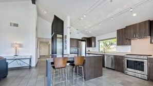 A modern kitchen with dark wood cabinets, stainless steel appliances, and a central island with bar stools. - Kai Entire Home (5 bedroom / 5 bath) (Carlsbad)