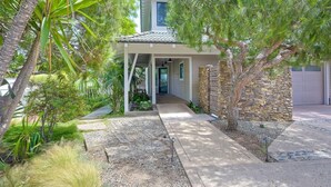 A modern house with a covered porch, stone wall, and a driveway leading to a garage. - Kai Entire Home (5 bedroom / 5 bath) (Carlsbad)