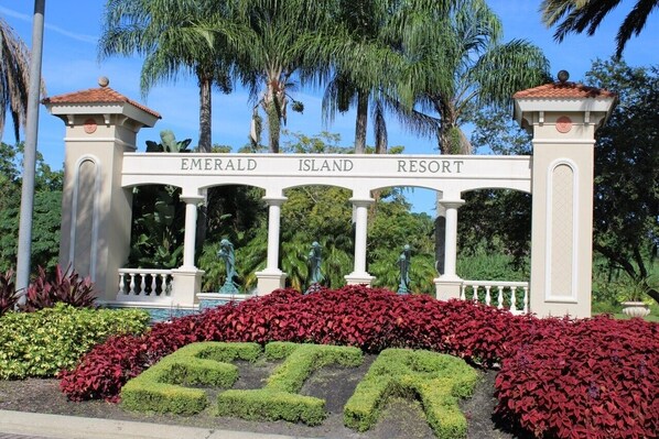 Señal de Emerald Island Resort con un arco blanco y columnas, rodeado de exuberante follaje y palmeras.