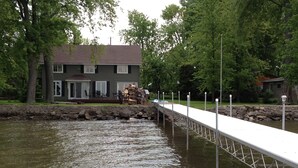 A riverside dock extending into a body of water, with a house and trees in the background. - Cozy Lake Winnebago Cottage: Shallow Sandy Shore, Close to EAA & Packers Games (Menasha)