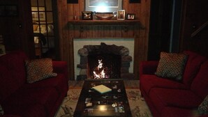 A cozy living room with a fireplace, two red armchairs, and a coffee table. - Cozy Lake Winnebago Cottage: Shallow Sandy Shore, Close to EAA & Packers Games (Menasha)