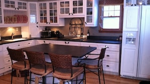 A kitchen with white cabinets, a central island with chairs, a microwave, and a wine bottle. - Cozy Lake Winnebago Cottage: Shallow Sandy Shore, Close to EAA & Packers Games (Menasha)