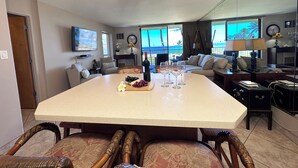 Un amplio salón con un gran comedor, asientos cómodos, una lámpara moderna y vistas al océano a través de amplios ventanales.