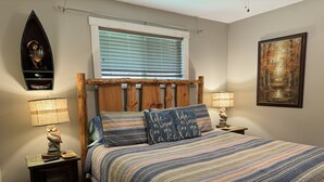 A bedroom with a wooden headboard, a striped bedspread, two bedside lamps, a nightstand, a framed picture on the wall, and a window with blinds. - Dancing Bream, Lakefront, Dock, Sun Deck, kayaks, Hot tub. (Hiawassee)