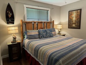 A bedroom with a wooden headboard, a striped bedspread, two bedside lamps, a nightstand, a framed picture on the wall, and a window with blinds. - Dancing Bream, Lakefront, Dock, Sun Deck, kayaks, Hot tub. (Hiawassee)