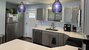 A modern kitchen with stainless steel appliances, a white countertop, and blue-striped pendant lights. - Dancing Bream, Lakefront, Dock, Sun Deck, kayaks, Hot tub. (Hiawassee)