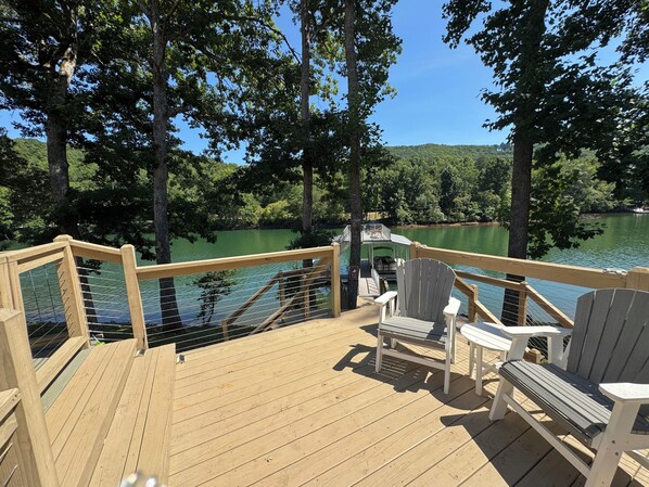A wooden deck with chairs overlooking a lake, surrounded by trees.