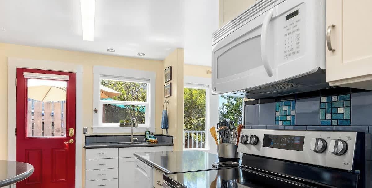 Una cucina moderna con una porta rossa, mobili bianchi, un forno a microonde e un fornello.