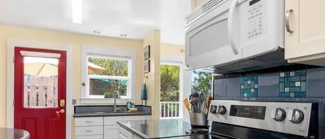 Una cucina moderna con una porta rossa, mobili bianchi, un forno a microonde e un fornello.