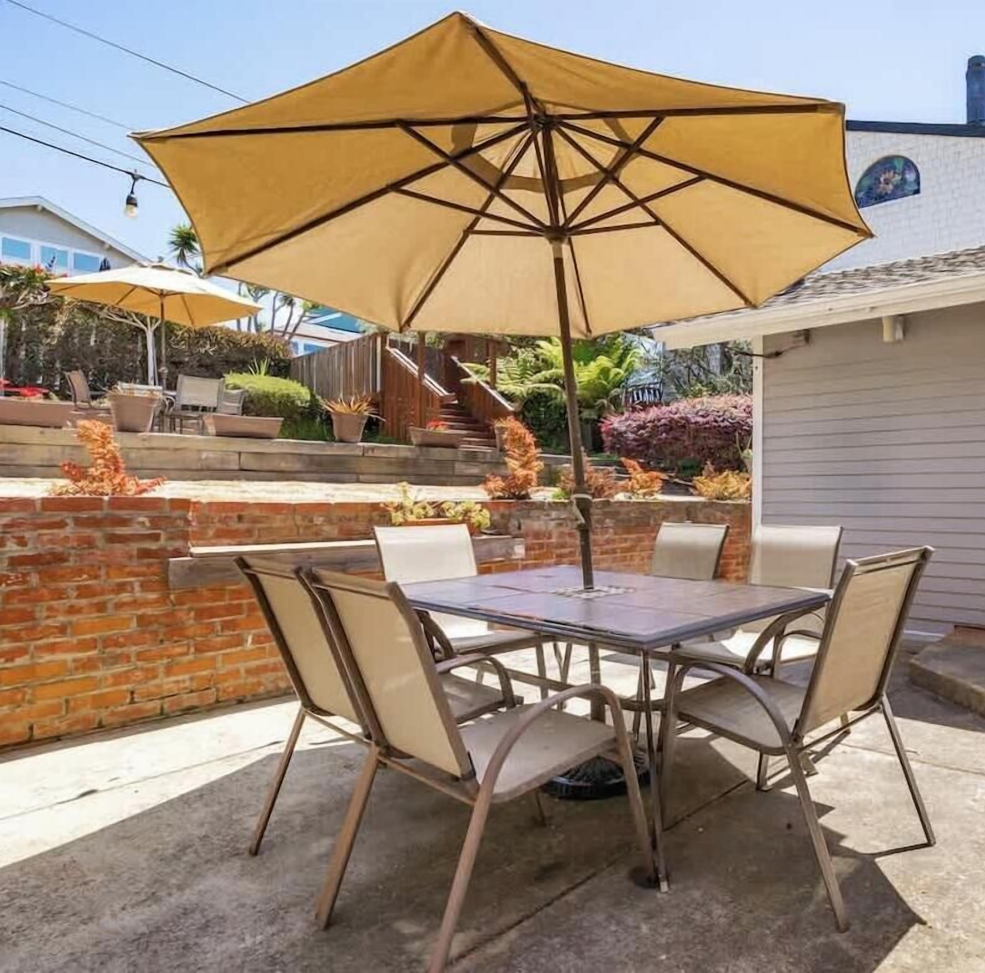 An outdoor patio with a table and chairs, a large umbrella, and a brick wall.