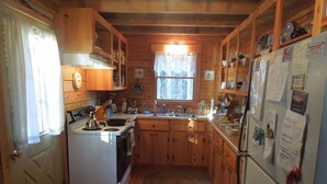 A cabin-style kitchen with wooden cabinets, a stove, sink, and a refrigerator. - Come, relax, and enjoy true peace and beauty. (Milbridge)
