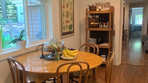 A dining area with a wooden table and chairs, a window with a view of the outside, a wall-mounted shelf with kitchen items, and a hallway leading to another room. - Tranquil and Spacious Cottage close to South Haven Beaches and Downtown (South Haven)