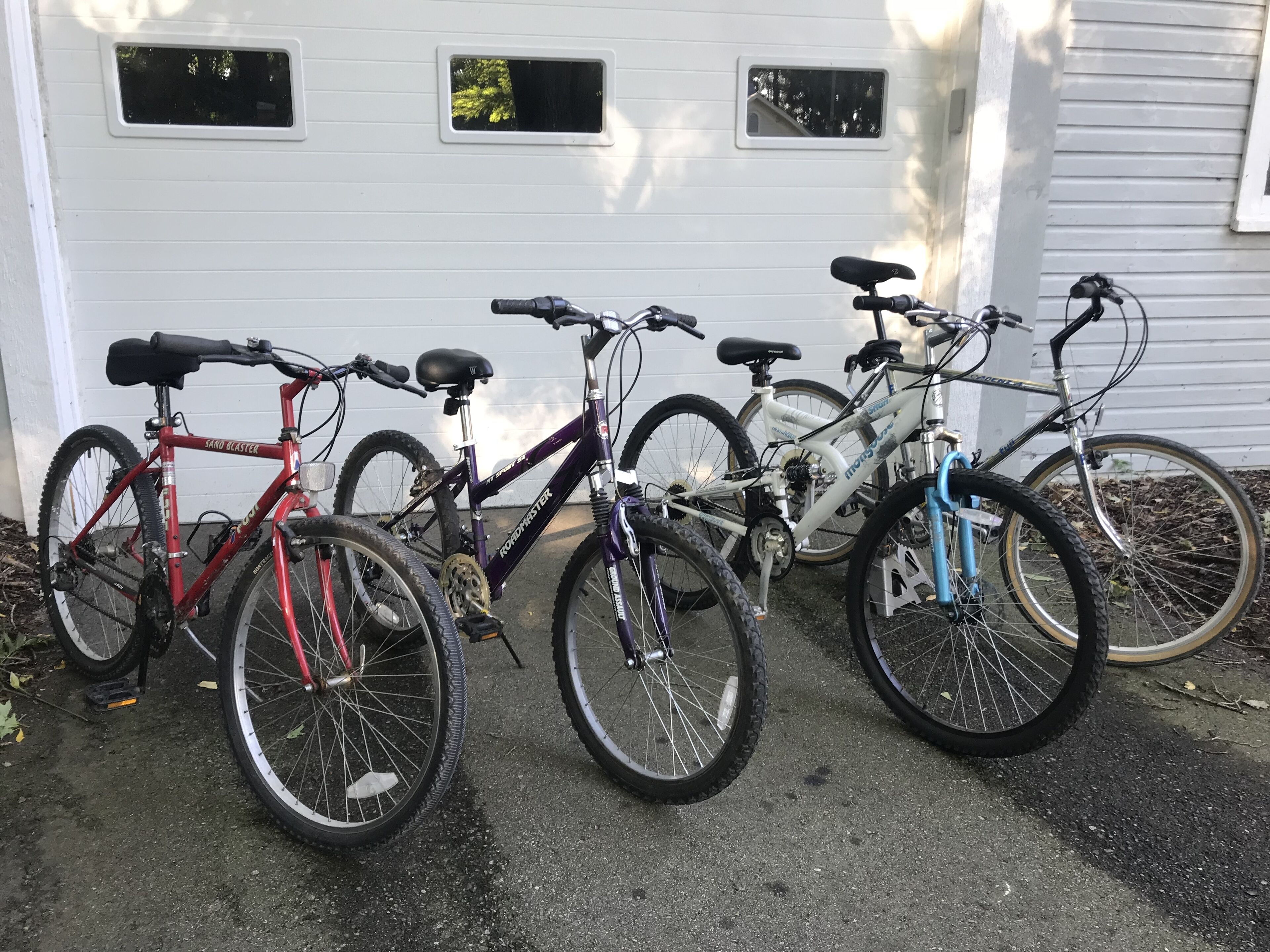 Tres bicicletes aparcades davant d'un garatge blanc amb tres finestres.